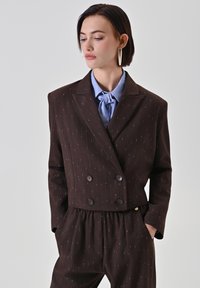 Braunes, zweireihiges Sakko mit Nadelstreifen, in einer maßgeschneiderten Passform, kombiniert mit einem hellblauen Hemd und passenden Hosen.