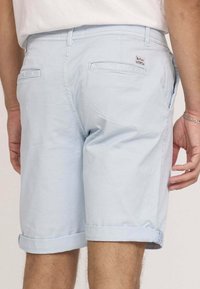 Shorts en coton bleu clair avec un ourlet roulé, des poches arrière et une étiquette tissée. Texture lisse avec une coupe décontractée.