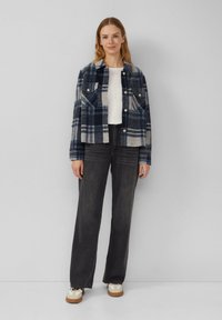 Giacca a quadri in misto lana blu navy e grigio con due tasche sul petto, chiusura con bottoni e design cropped; abbinata a jeans scuri e sneakers.