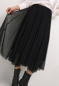Black tulle skirt with a pleated design. Semi-sheer texture featuring small floral patterns. Mid-calf length, paired with black ankle boots.