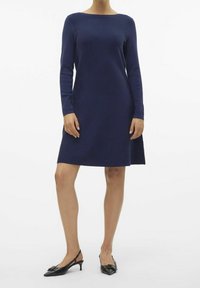 Marinblå långärmad klänning med båturringning, A-linjeformad, tillverkad av ett slätt tyg. Matchad med svarta slingbacks med rosettdetalj.