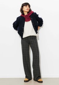 Veste à fines rayures bleu marine portée sur un pull en maille blanc, avec un sweat à capuche bordeaux. Pantalon large à carreaux gris et chaussures plates beige.