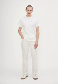Hvit bomulls-T-skjorte med et lite blått grafisk design, kombinert med lyse beige chinos og hvite sneakers med brune såler.