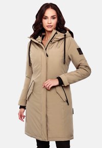 Beige padded parka with a hood, black accents, zippered pockets, and a soft texture. Features a logo patch on the sleeve.