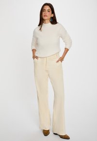 Crème gebreide trui met een hoge hals, gecombineerd met lichtbeige wijde corduroybroek. Bruine suède enkellaarzen.