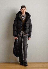Doudoune noire, gilet en tricot vert, chemise à imprimé léopard, jeans gris évasés, portant un sac noir texturé, associé à des chaussures noires.