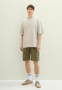 Beżowy, oversize'owy t-shirt, oliwkowe szorty cargo, kremowe sneakersy i białe skarpetki w czarne paski. Prosty, luźny i funkcjonalny zestaw ubrań.