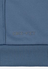 Blå Dri-FIT stof med en glat tekstur og ribbet kant. Logoet "DRI-FIT" i en mørkere skygge er placeret på fronten.