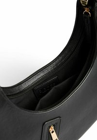 Bolso de mano de cuero negro con herrajes dorados, que cuenta con un bolsillo con cremallera y un diseño suave y estructurado. El interior muestra detalles de forro y costura.