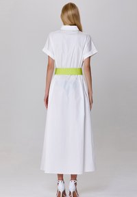 Robe maxi en coton blanc à manches courtes, dotée d'une ceinture verte à la taille. La vue de dos met en valeur la silhouette fluide de la robe.
