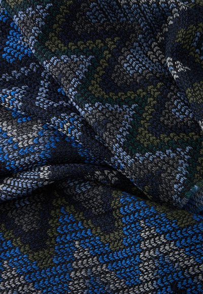 Gros plan d’un tissu tissé plié montrant des motifs en zigzag en fils texturés bleus, gris, verts et noirs.