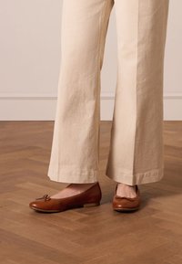 Brown leather ballet flats with a bow detail, solid color, low heel, and smooth texture, paired with beige wide-leg pants on wood flooring.