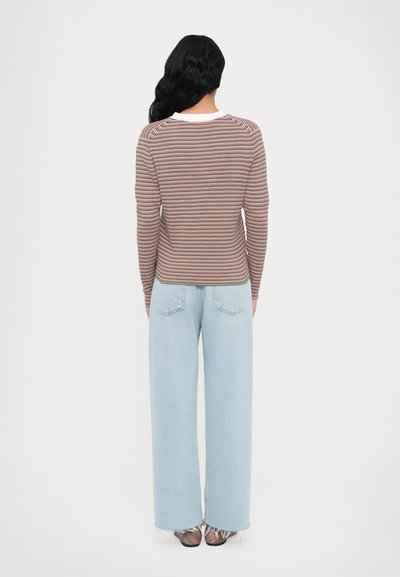 Striped long-sleeve shirt in brown, orange, and blue with a white collar. Paired with light blue wide-leg jeans and patterned shoes.