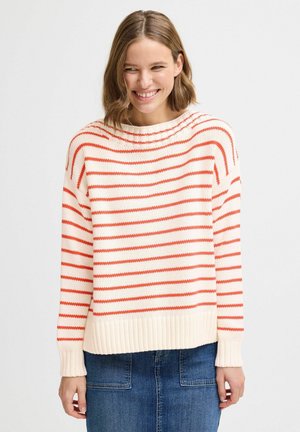 Pull en maille couleur crème avec des rayures horizontales rouges. Col rond, poignets et ourlet côtelés, coupe décontractée. Porté avec une jupe en denim.