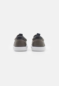 Graue Leder-Sneaker mit einer weißen Gummisohle, ausgestattet mit einer schwarzen Fersenkappe und einem Zugtab für einfaches An- und Ausziehen. Glatte Textur und minimales Design.