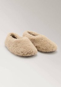 Pehmeät, beige, pörröiset tossut suljetulla varvasdesignilla, aseteltuna vierekkäin neutraalilla taustalla.