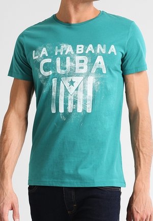 Homme portant un t-shirt turquoise avec le texte blanc "La Habana Cuba" et une étoile à l’intérieur d’un dessin en forme de triangle au centre.