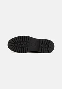 Suela de zapato de goma negra con surcos y patrones profundos para agarre. Presenta una superficie lisa y plana con bordes redondeados.