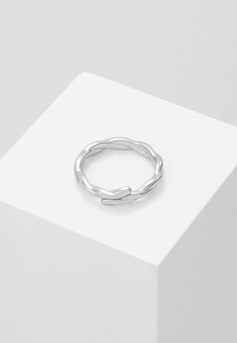 Sølvvridd ring med en jevn, blank finish og fletterdesign, vist på en minimalistisk hvit pedestal.