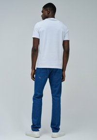 Jeans de mezclilla azul y una camiseta blanca lisa. Los jeans tienen un corte clásico, con cinco bolsillos y detalles de costura sutiles.
