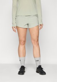 Shorts de sport vert clair avec une texture lisse, associés à des chaussettes grises ornées d'imprimés et des baskets de course noires.