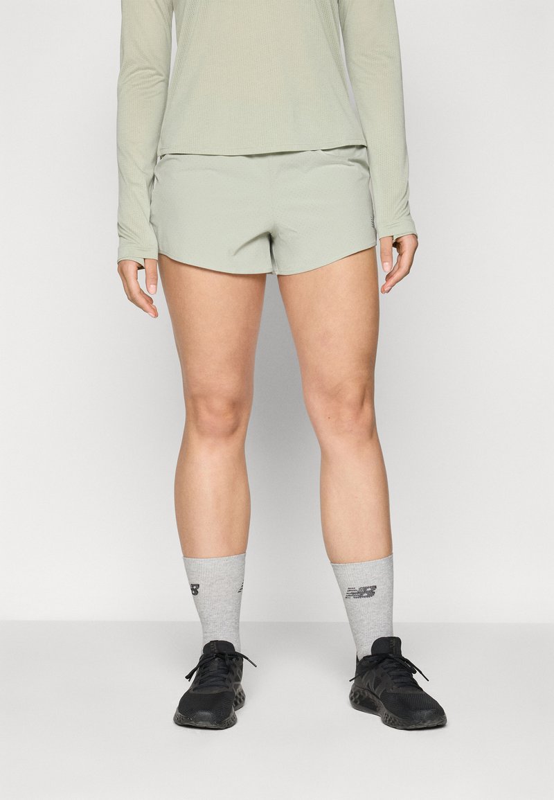 Shorts de sport vert clair avec une texture lisse, associés à des chaussettes grises ornées d'imprimés et des baskets de course noires.