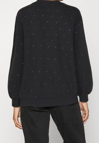 Černá mikina s kulatým výstřihem, nadýchanými rukávy a rozptýlenými stříbrnými ozdobami. Měkká látka a volný střih.