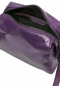 Lila Ledertasche mit glatter Textur, Reißverschlussöffnung und lässigem Design. Innenausstattung mit einfarbigem dunklem Futter. Verstellbarer Riemen sichtbar.