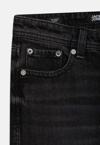 Blugi negri din denim cu croială lejeră. Au elemente metalice argintii, design cu cinci buzunare și material texturat cu un model subtil.