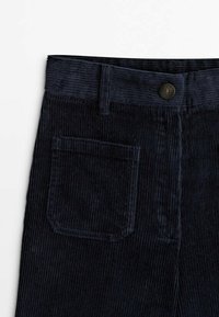Pantalon en velours côtelé bleu foncé avec une poche avant, des passants pour ceinture et une fermeture à bouton à la taille sur fond blanc.