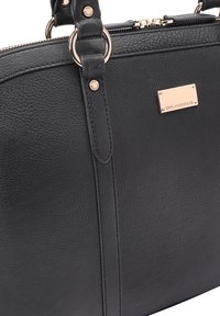 Zwarte leren handtas met textuur, goudkleurige hardware, dubbele rits en een klein rechthoekig logo schild.