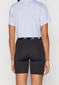 Camiseta lila cortada combinada con pantalones cortos deportivos negros ajustados que presentan una cinturilla de marca y una textura suave.
