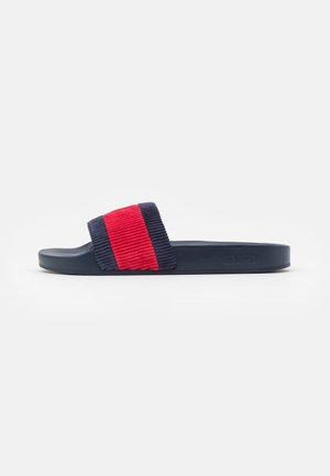 Marineblauwe slippers met een geribbelde strap in rood en blauw. Zacht, textuur materiaal met een platte zool en een merkdetail aan de zijkant.
