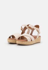 Sandales à talons compensés en cuir beige avec un design à brides croisées, une plateforme en jute tressé et un accent en métal doré sur la bride de cheville réglable.