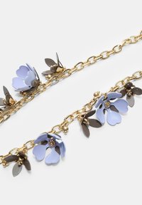 Zlatonosna verižica z večplastnimi modrimi cvetnimi obeski, okroglimi kroglicami in temno zelenimi listi, ki prikazuje gladko teksturo in zapleteno detajlnost.