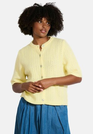 Cardigan en tricot jaune à manches courtes, avec un motif texturé et un col rond, comportant cinq boutons sur le devant.
