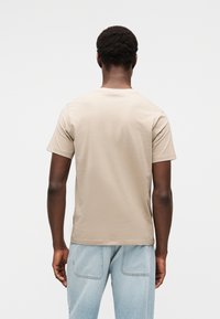 Μπεζ κον τομάνικο μπλουζάκι με στρογγυλό λαιμόκοψη, με λεία υφή και ίσια κοπή, συνδυασμένο με ανοιχτό μπλε τζιν.