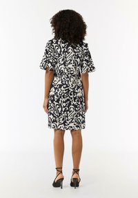 Schwarzes und weißes gemustertes Kleid mit kurzen, ausgestellten Ärmeln, knielangem Schnitt und taillierter Taille, kombiniert mit schwarzen, schnürbaren High Heels.