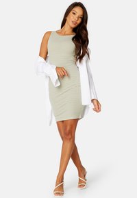 Vestito senza maniche, aderente, in verde chiaro e con righe bianche, abbinato a una camicia bianca aperta con bottoni. Tessuto morbido e lunghezza fino al ginocchio.