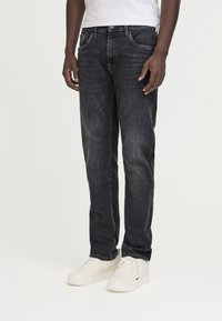 Dark wash denim jeans with a straight leg design, featuring front pockets and a top button closure, paired with white sneakers.