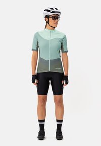 Maillot de cyclisme vert menthe à manches courtes, avec fermeture éclair sur le devant et motif géométrique. Assorti à un short de cyclisme noir et des chaussettes coordonnées.