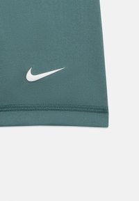 Teal-kangas, jossa on näkyvät ompeleet ja valkoinen Nike-swoosh-logo lähellä alareunaa.