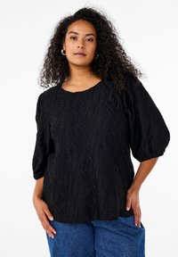 Black textured top with a wave pattern, featuring a round neckline and puffed sleeves. Paired with blue denim shorts.