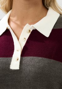 Stickad pikétröja med maroon, grå och krämfärgade horisontella ränder, en krämfärgad krage och tre knappar fram. Mjuk textur.