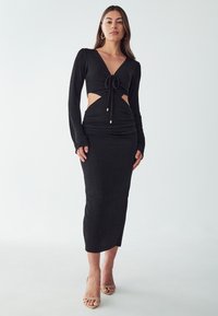 Black long-sleeve dress with a V-neck, cut-out waist, and gathered skirt detail. Made from soft, textured fabric with gold accents.