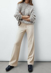 Beige wide-leg trousers paired with a textured gray sweater. Shoes are dark clogs. The background is neutral, emphasizing the outfit.