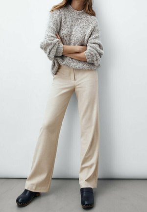 Beige wide-leg trousers paired with a textured gray sweater. Shoes are dark clogs. The background is neutral, emphasizing the outfit.