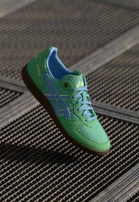 Grønne joggesko med blå detaljer, med en teksturert overdel, rund tå og brun gummisåle. Inkluderer buede striper på sidene.