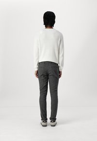 Suéter blanco de canalé, pantalones grises a medida y zapatillas negras. Vista desde atrás, con un fondo liso.