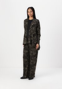 Leopardmönstrad kostym i mjukt tyg; lång, öppen cardigan med raka byxor. Färgpaletten inkluderar svart och tan. Minimalistisk design, avslappnad passform.